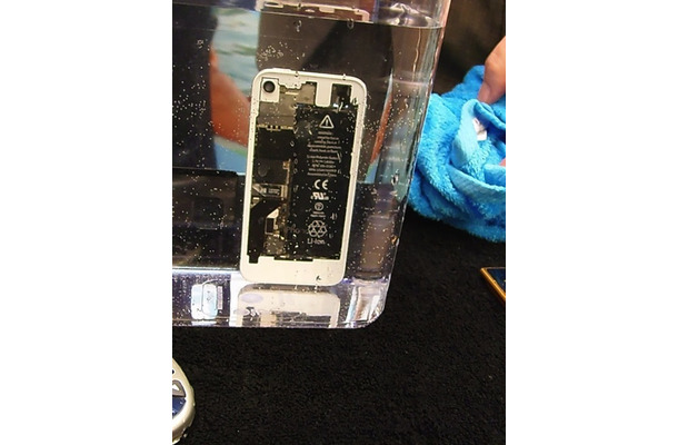 iPhoneの水没実験。iPhoneから泡が出ているので、内部に水が入っていることが分かる。透明で数ミクロンと薄いため分からないかもしれないが、電子部品にコーティングが施されているので、水が入っても安心