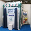 ハムロン・テックの防災倉庫「レスQbox」。今回の展示では公衆トイレとしても活用できるように倉庫壁面にカーテンレールを設置して、トイレ利用時にはカーテンで目隠しできるよう仕様となっていた（撮影：防犯システム取材班）