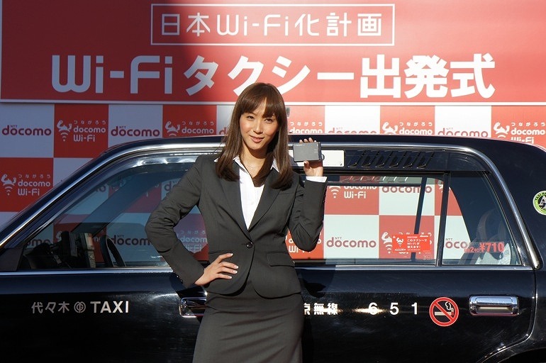 Wi-Fi搭載タクシーを前に、モバイルWi-Fiルータを手にする藤本美貴