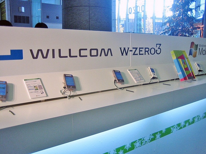 ウイルコムの体験コーナー。本日発売のW-OAM対応超小型通信モジュール「W-SIM」も展示されている。その他、NTTドコモとソフトバンクモバイルもそれぞれ体験コーナーを設け、担当スタッフが説明にあたる