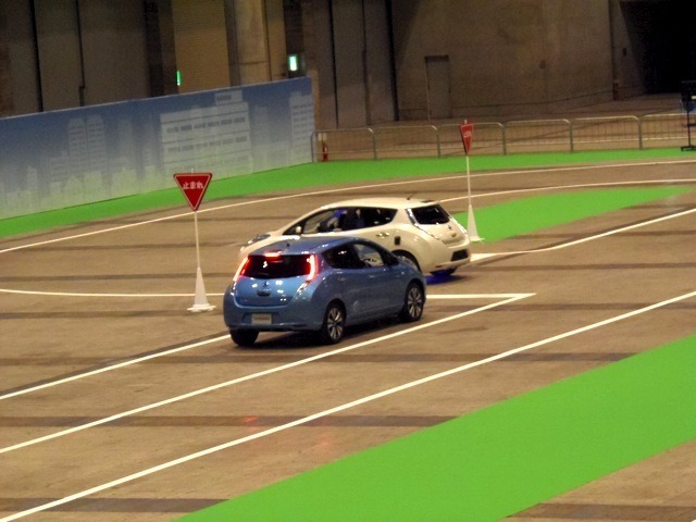 交差点でのシーン。青いクルマはドライバーがハンドルを握っている。白いクルマが自動運転車だ