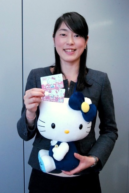 セディナカードを持つ広報部の樺島さん。紺×黄のセディナマスコットのキティちゃんと。こちらは非売品。