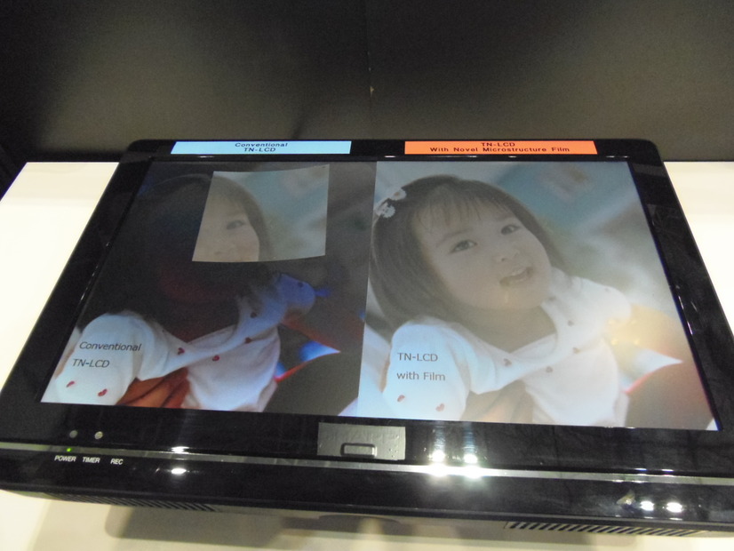 シャープのブースで展示されていた光学フィルム。液晶ディスプレイの上に乗せるだけで、どんな角度からでも画面がきれいに見える。写真右がフィルム適用時。写真左は一部フイルムを適用（顔の部分）。