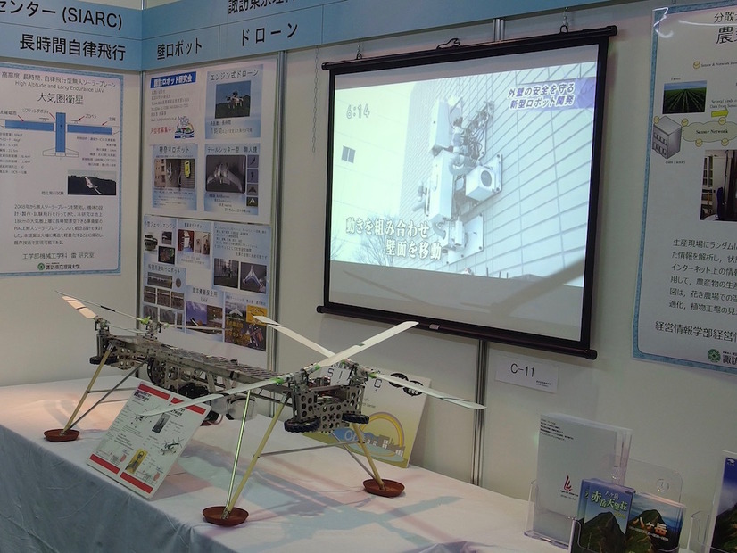 諏訪東京理科大学と諏訪産業集積研究センターの共同出展ブース。ディスプレイ内は壁走行ロボット