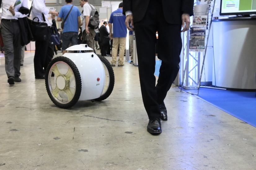 歩く人を追尾する様子。特殊ハブ機構と平行二輪機構により、その場での旋回や素早い方向転換が可能。時速20～30kmの高速走行でも車体の水平を維持できるという（撮影：防犯システム取材班）