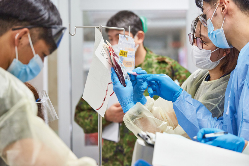 臨時の医療施設に運ばれてきた傷病者を治療する演習で、銃撃で負った傷により多量の血液が失われたという設定の模擬患者に輸血動作を行う自衛官