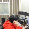 PCで録音トラックを確認するディレクターの伊藤氏（手前）と、曇りガラスの向こうに声優の永吉さん