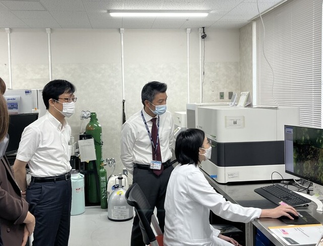 ゲノム医療総合推進センターでの解析機器について説明を受ける井上諭一局長(左)